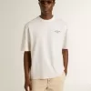 Camiseta unisex blanca con estampado mediterráneo y parche dorado Pescheria en la manga Camiseta unisex blanca con estampado mediterráneo y parche dorado Pescheria en la manga